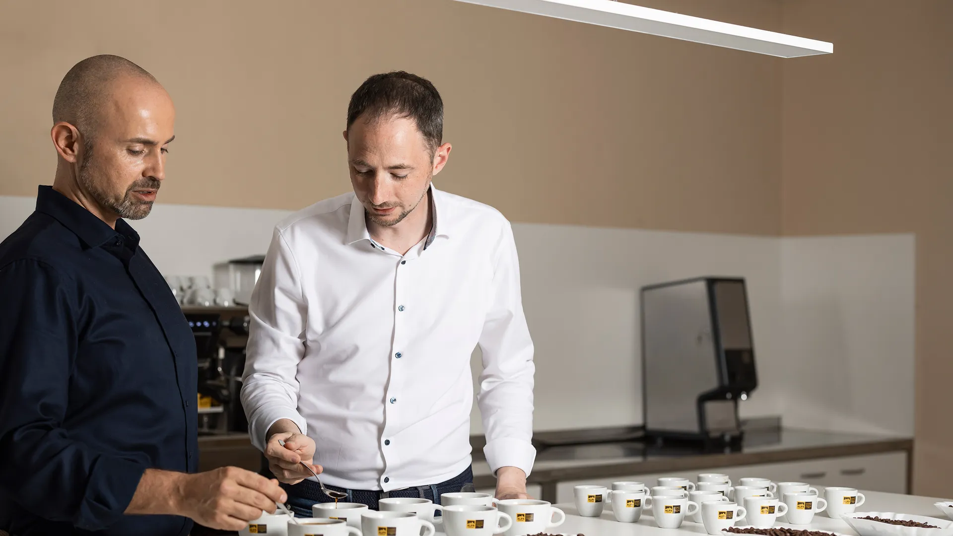 Due uomini eseguono un cupping professionale di caffè con tazze Alps Coffee a un tavolo bianco