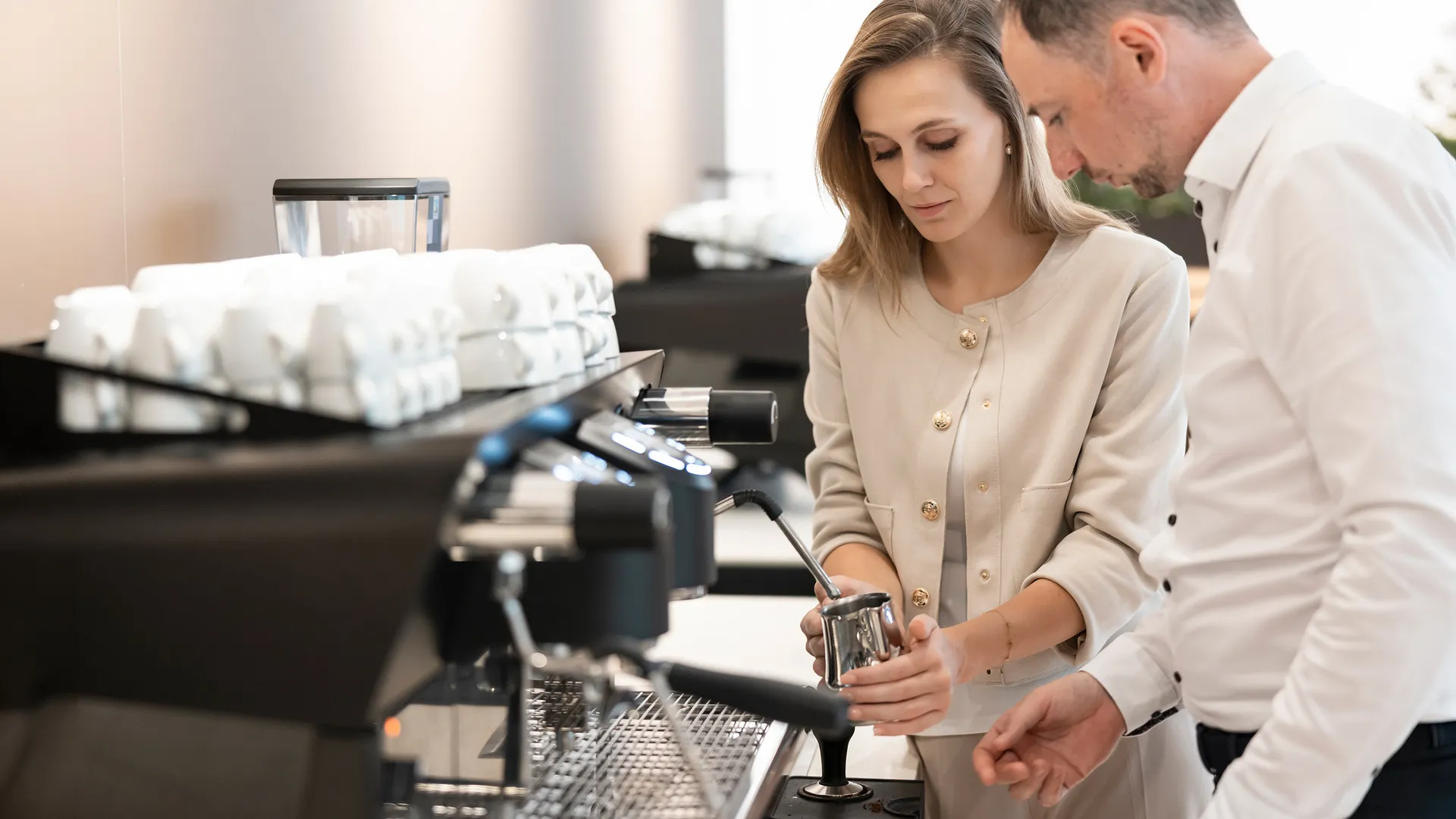 Frau und Mann üben Milchaufschäumen an professioneller Siebträgermaschine im Alps Coffee Training