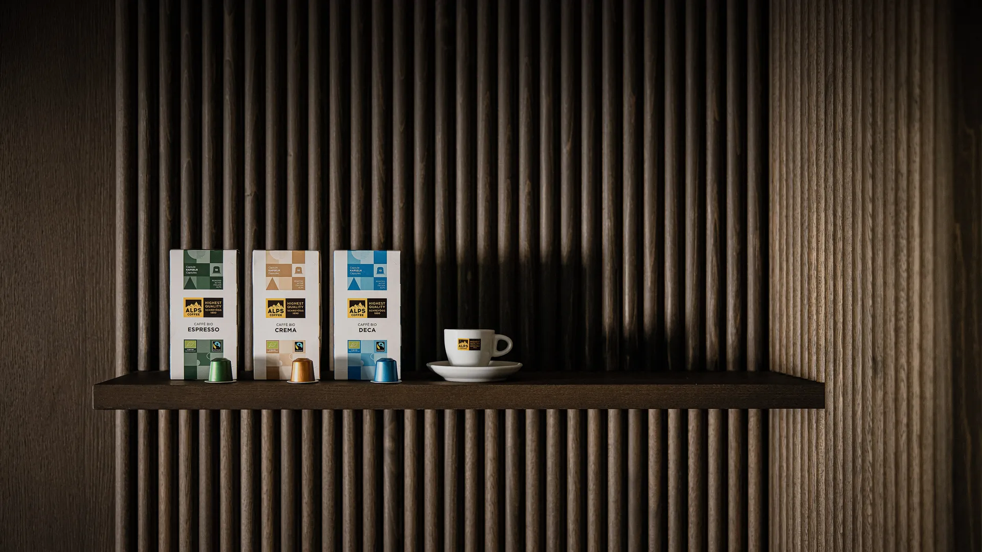 Alps Coffee organic capsules Espresso, Crema and Deca on dark wood shelf with Alps Coffee espresso cup