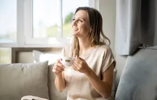 Smiling woman sitting relaxed on sofa, holding Alps Coffee cup and gazing contentedly out the window