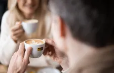 Man holding Alps Coffee cup with latte art, smiling woman with cappuccino in background