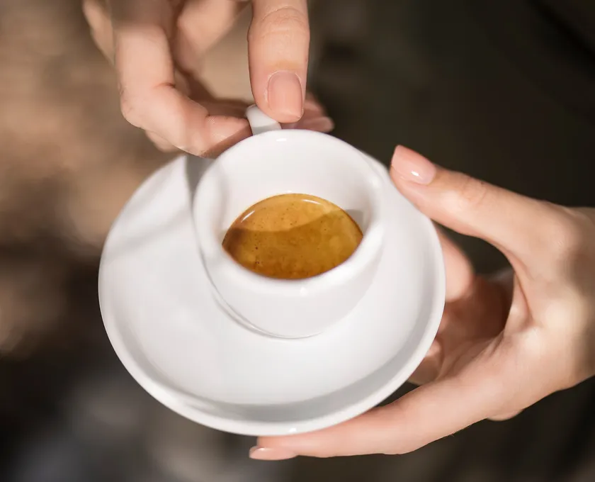 Woman's hands holding a white espresso cup with golden crema viewed from above