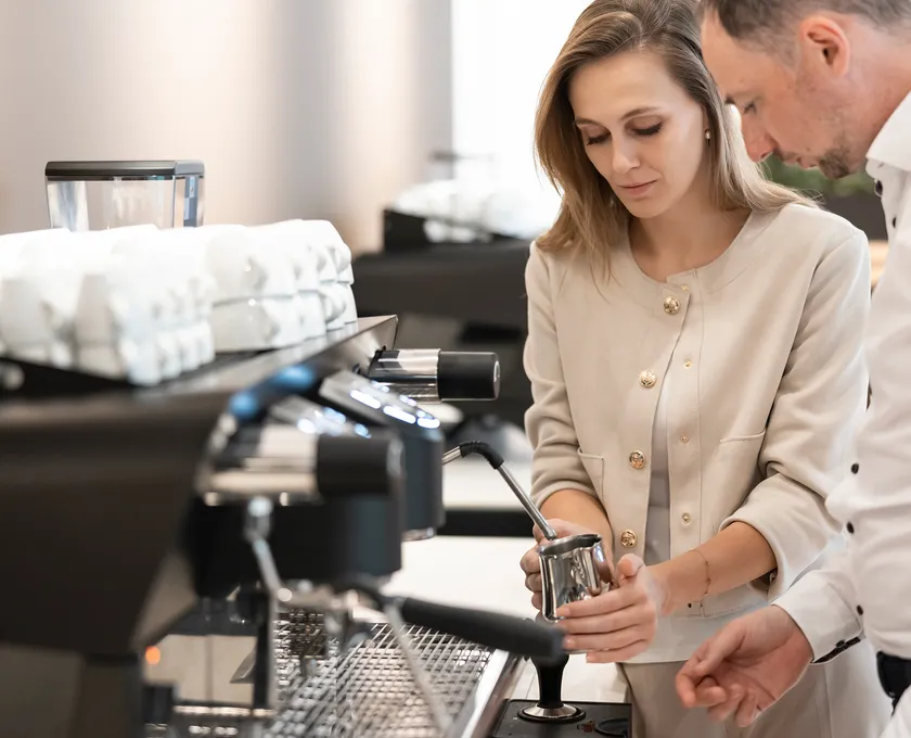 Woman and man practicing milk steaming on professional espresso machine at Alps Coffee training
