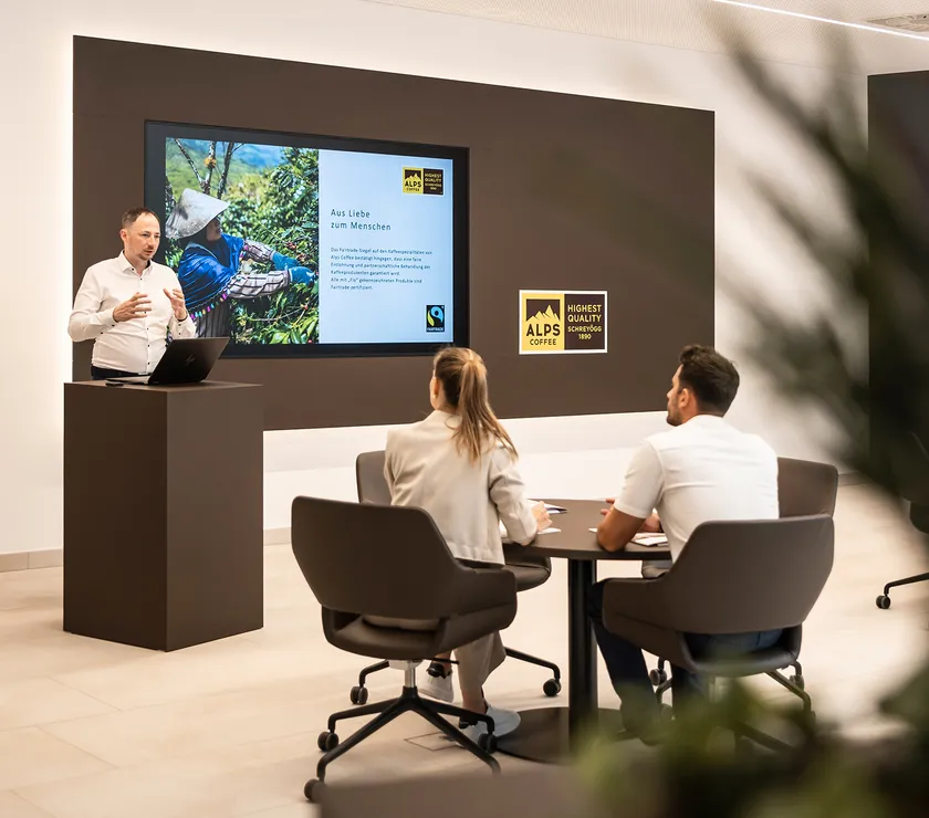 Alps Coffee employee presenting Fairtrade training in modern seminar room with screen and Alps Coffee logo