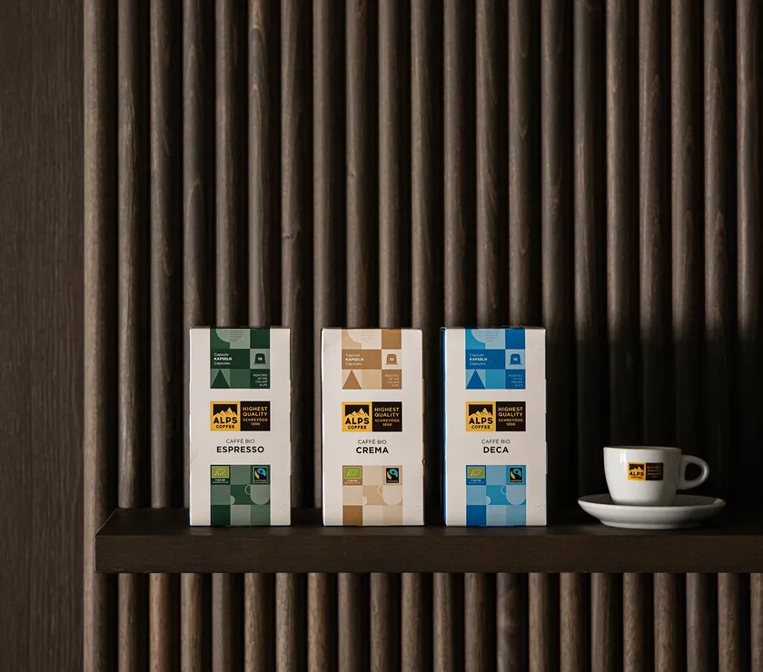 Alps Coffee organic capsules Bio Espresso, Crema and Deca on dark wood shelf with espresso cup beside